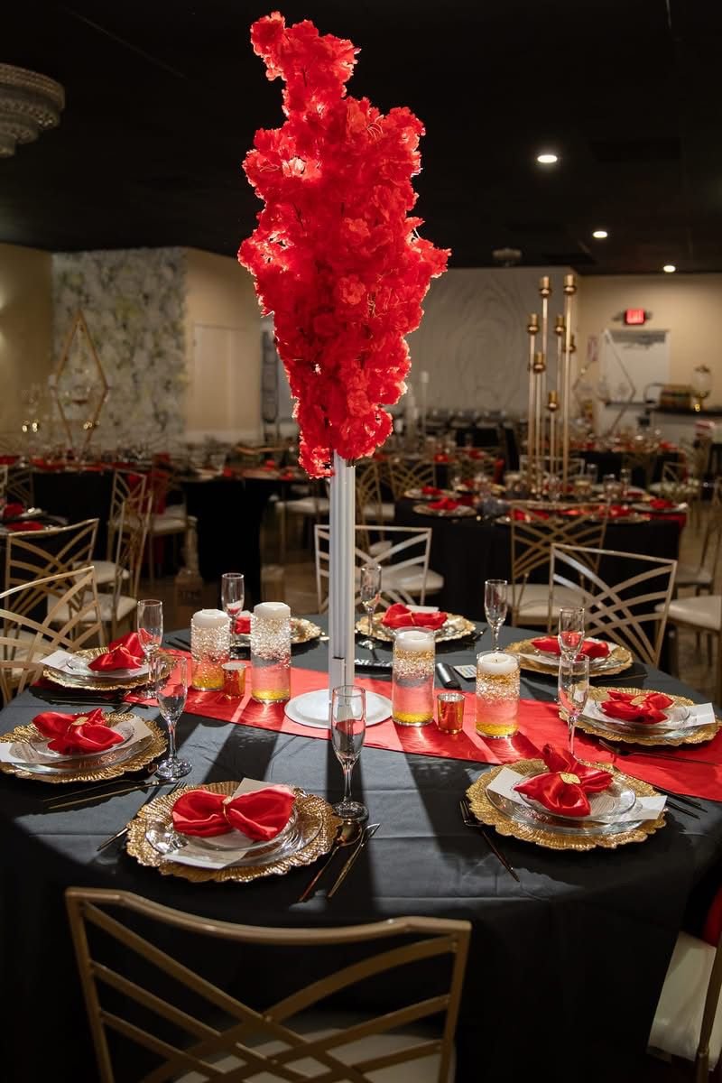 Tall red blossom centerpiece rising over a black and gold table in a full ballroom